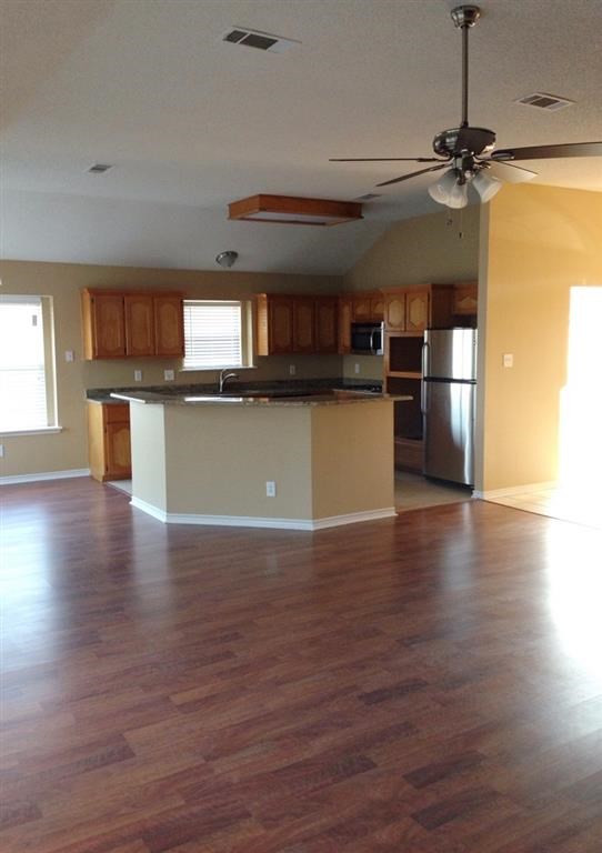 an empty living room with a kitchen and a ceiling fan