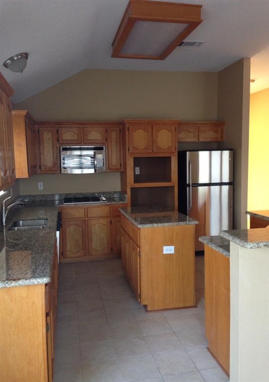 an empty kitchen with wooden cabinets and a refrigerator