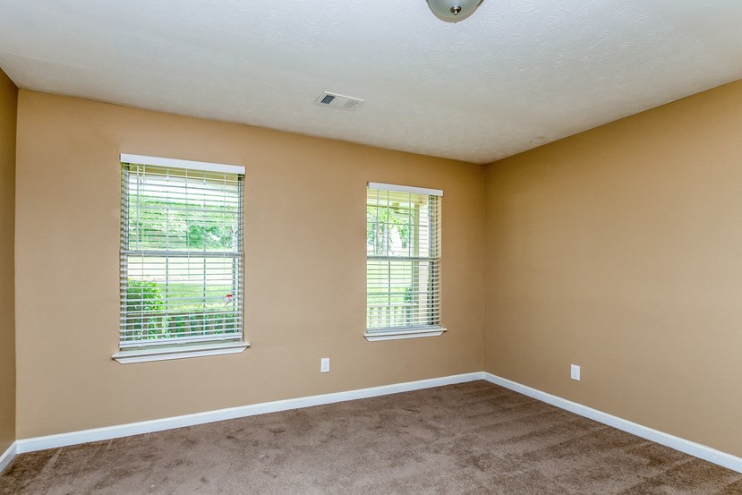 an empty living room with two windows and a carpet