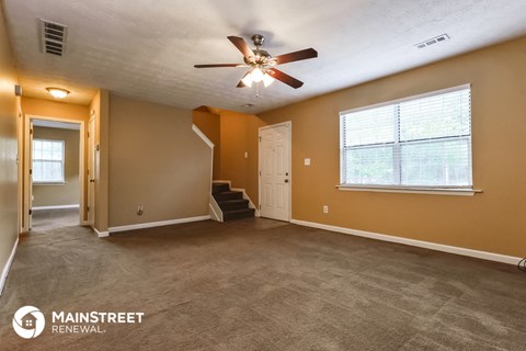 the living room of a house with carpet and a ceiling fan