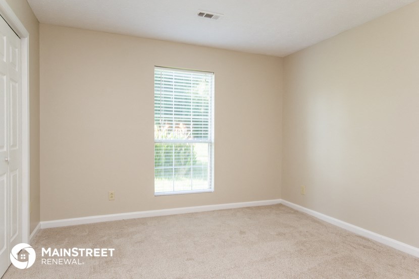 a bedroom with a large window and beige carpet