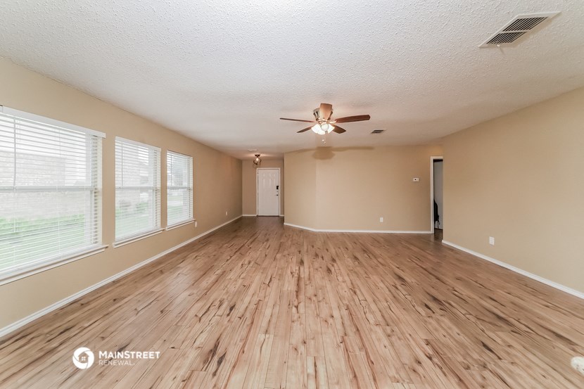 the spacious living room with wood flooring and a ceiling fan