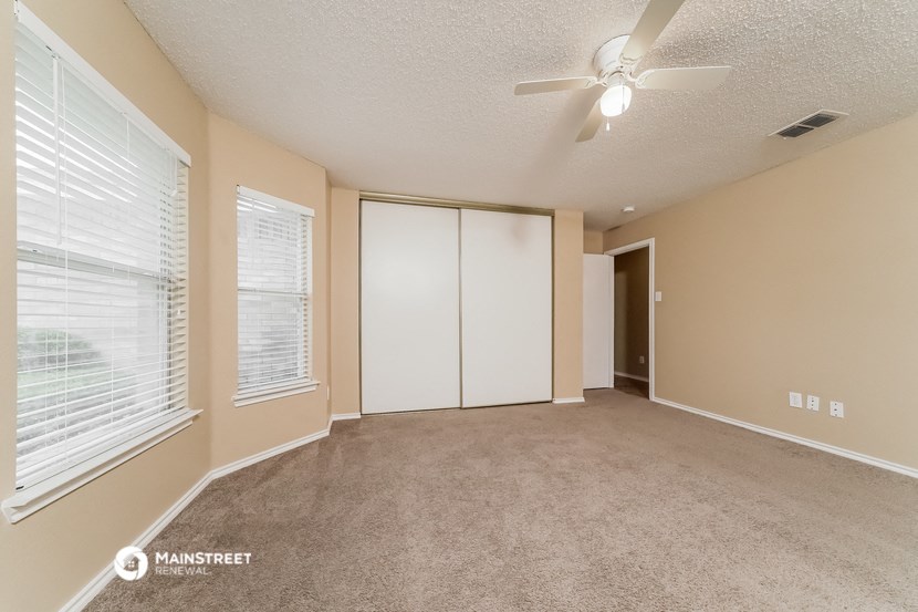an empty living room with a large window and a ceiling fan