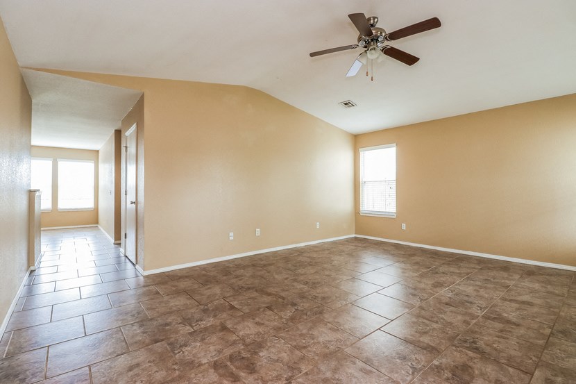an empty living room with a ceiling fan and tiled floors