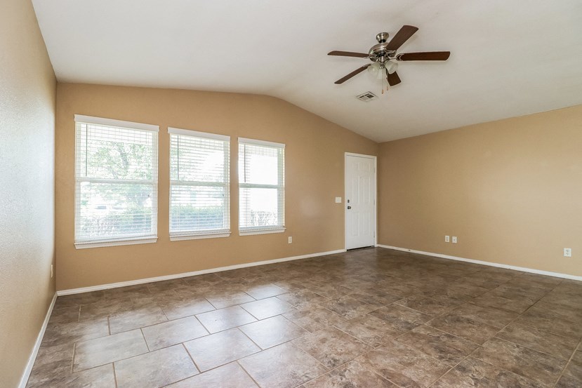 an empty living room with a ceiling fan and windows