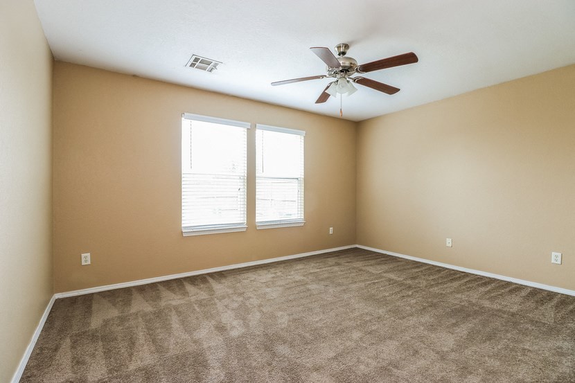 an empty living room with a ceiling fan and two windows
