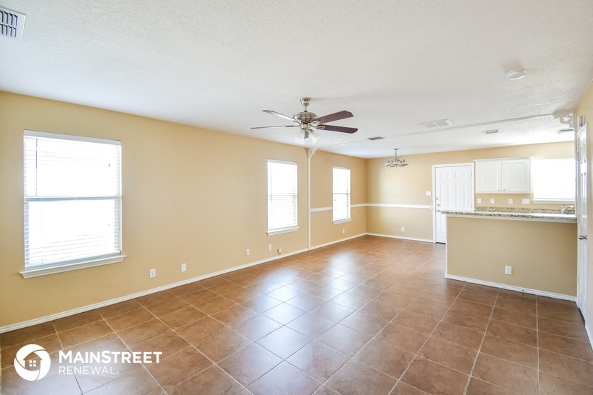 an empty living room with a kitchen and a ceiling fan