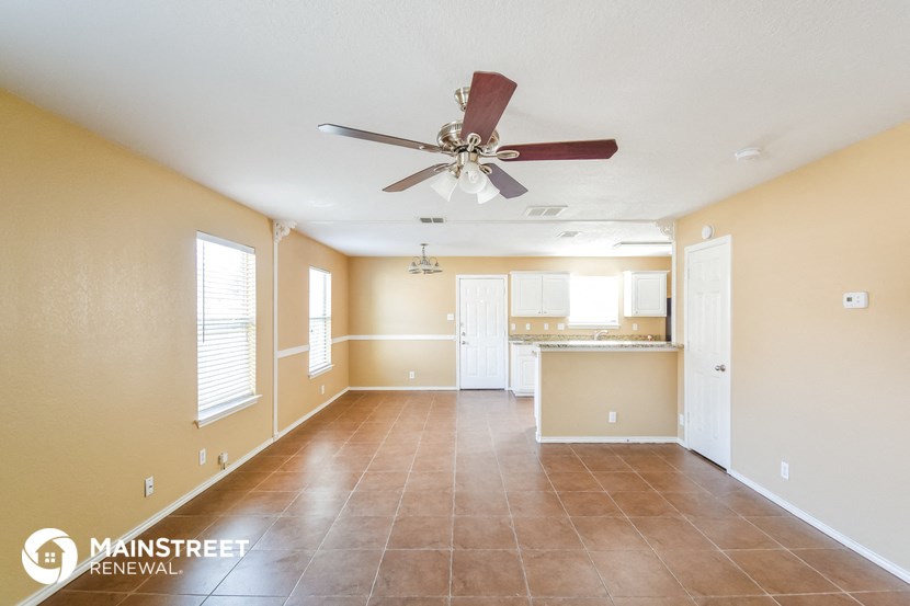 an empty living room with a ceiling fan and a kitchen