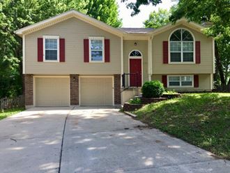a tan house with a driveway and a red door