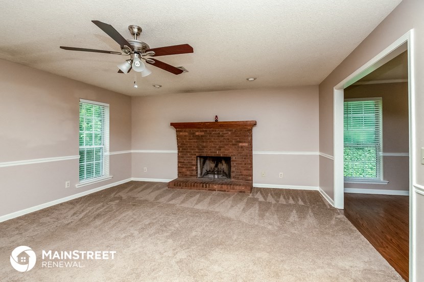 an empty living room with a brick fireplace and a ceiling fan
