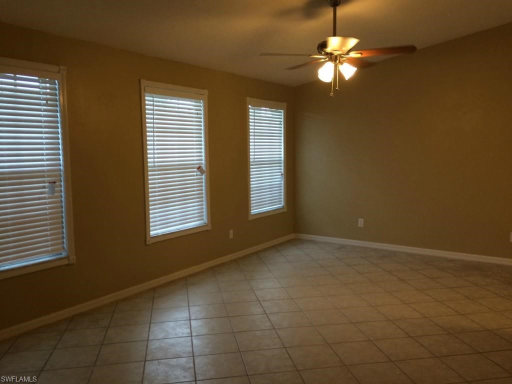 an empty living room with a ceiling fan and three windows