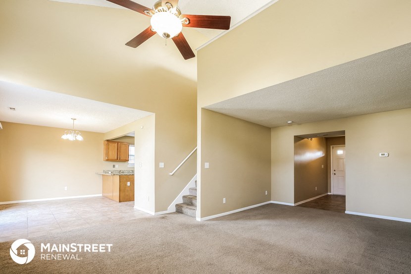 an empty living room with a ceiling fan and a kitchen
