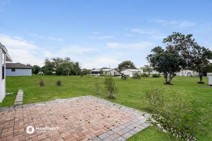 a backyard with a brick patio and a grassy field with houses in the background