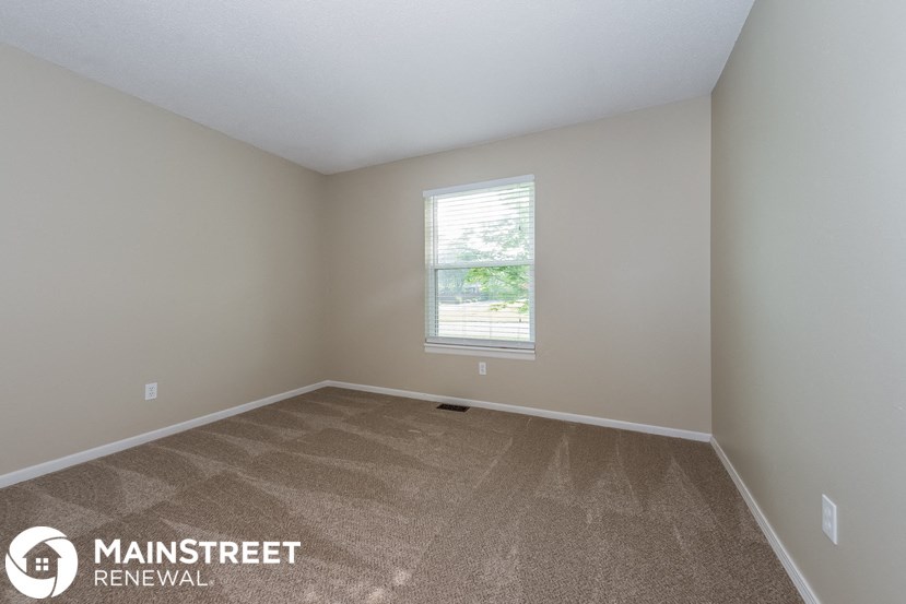 the spacious bedroom with carpeted flooring and a window