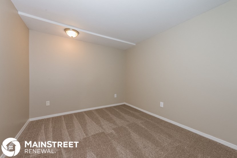 the spacious living room with carpeted flooring and white walls