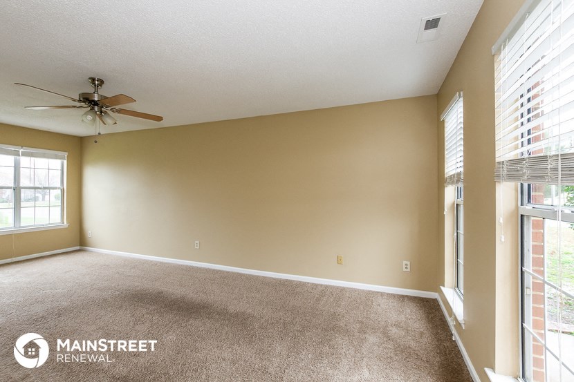 an empty living room with a ceiling fan and large windows
