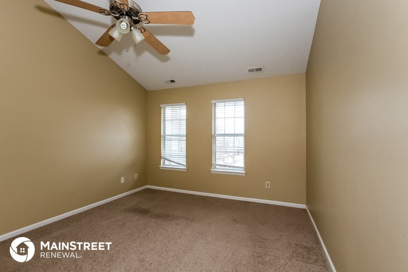an empty room with a ceiling fan and two windows