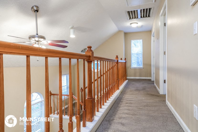 a long hallway with a wood railing and a ceiling fan