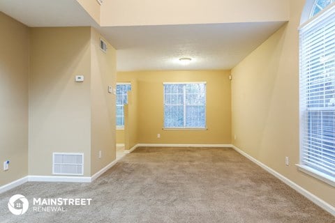 a spacious living room with carpet and two windows