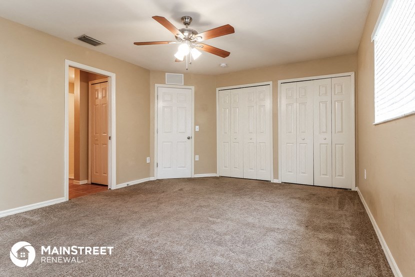 the living room is carpeted and has a ceiling fan
