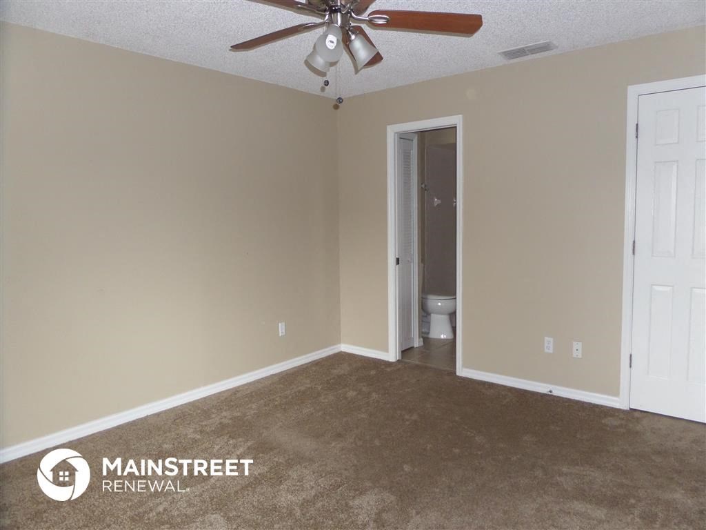 an empty living room with a ceiling fan and a door to the bathroom
