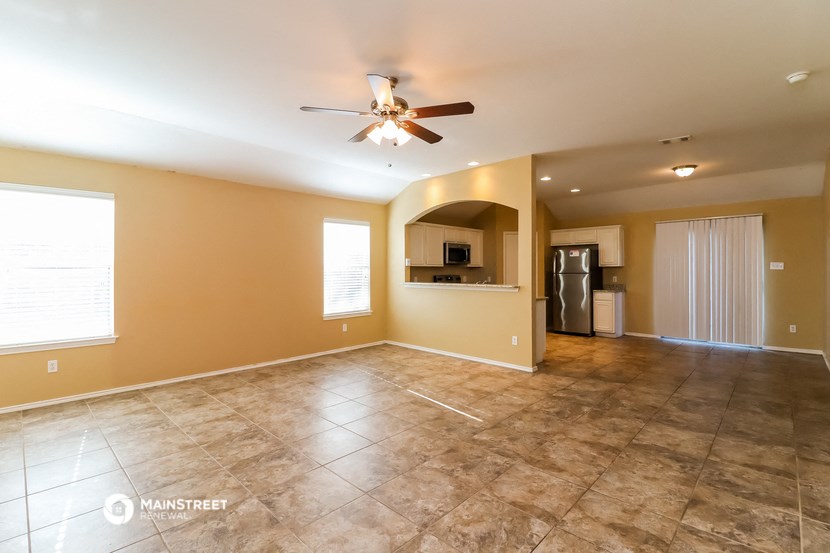 an empty living room with a ceiling fan and a kitchen