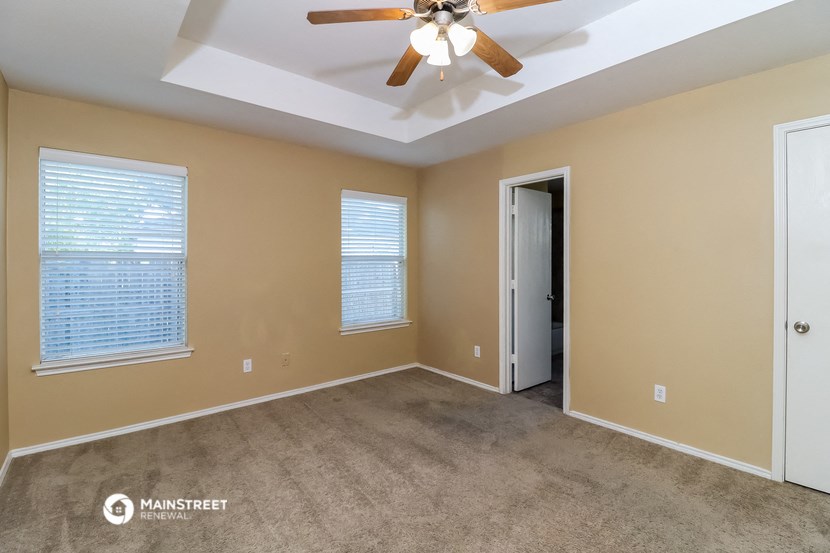 an empty living room with a ceiling fan and two windows