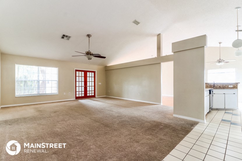 an empty living room with a red door and a kitchen
