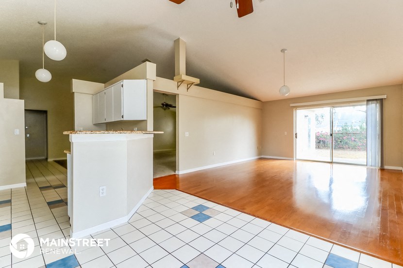 an empty living room with a kitchen and a hard wood floor