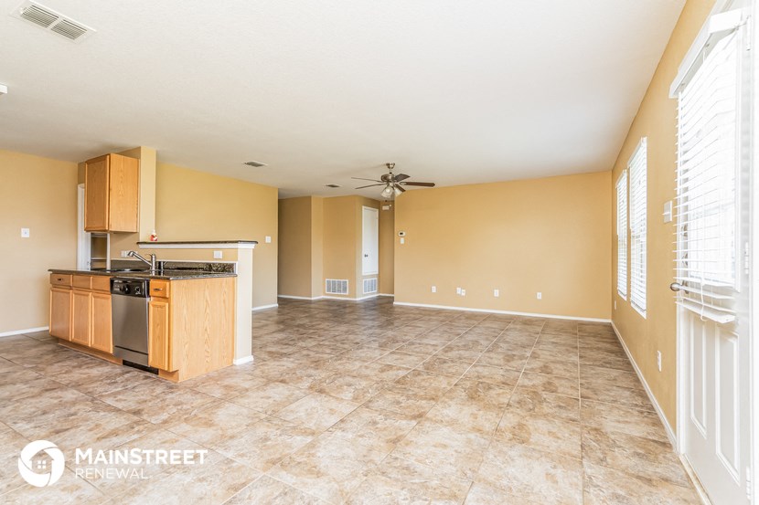 an empty living room with a kitchen and a ceiling fan