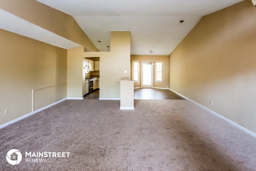 an empty living room with carpet and a kitchen