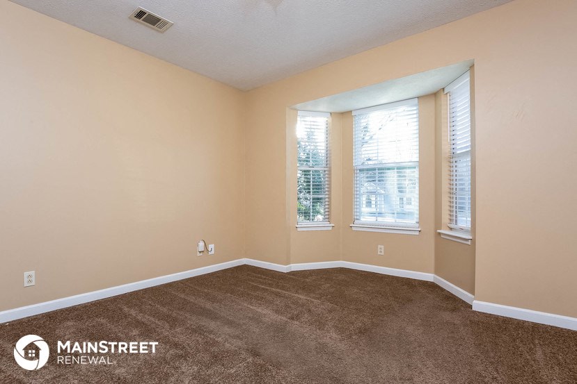 the living room of a home with carpet and three windows