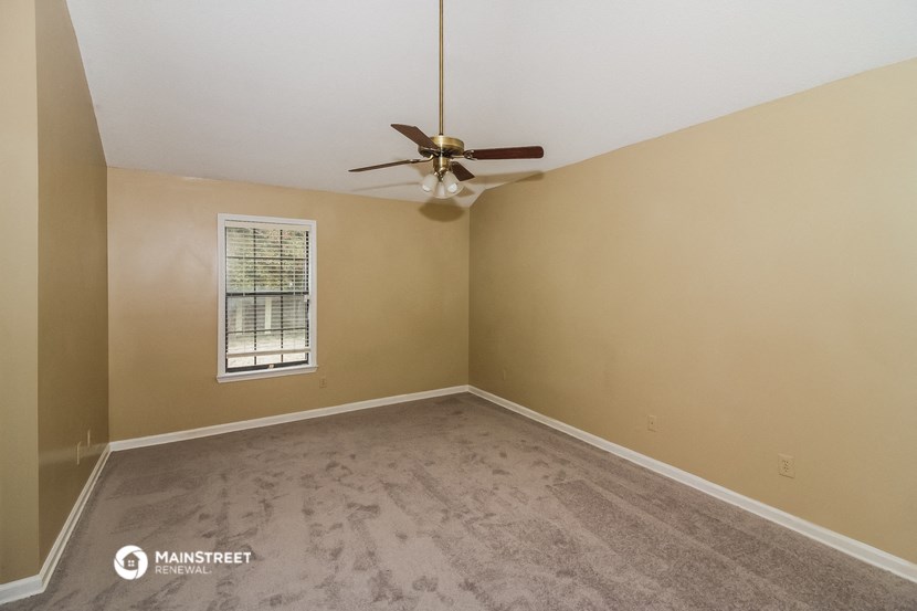 the spacious living room of an empty home with a ceiling fan