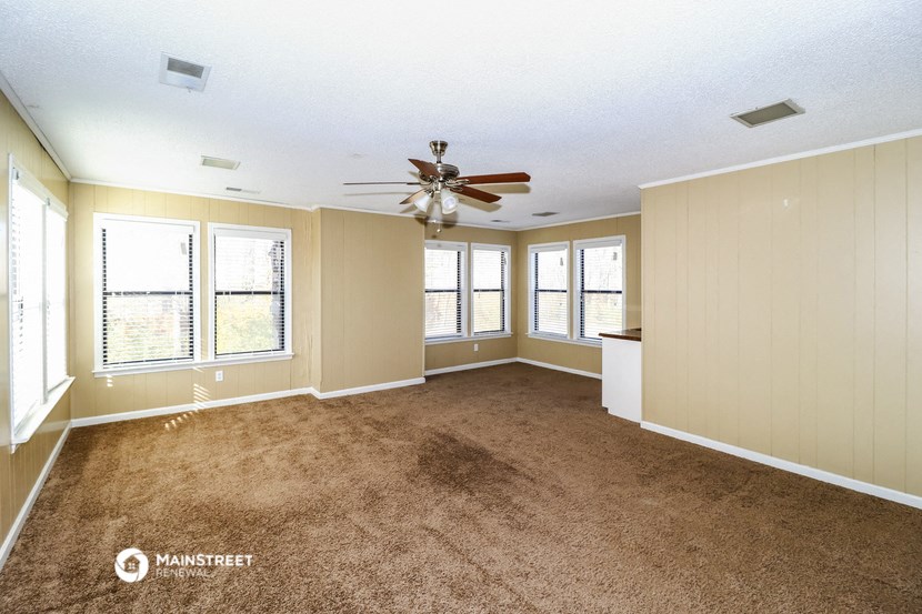 an empty living room with a ceiling fan and windows