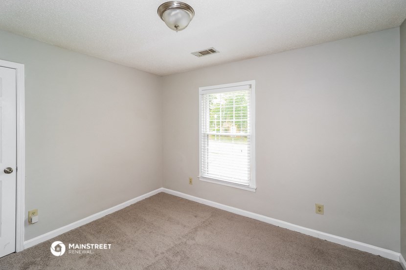 the spacious bedroom with carpeted flooring and a window