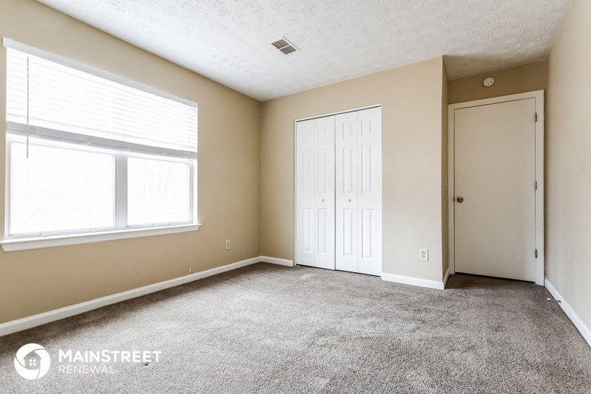 the living room of an apartment with a carpeted floor and two windows