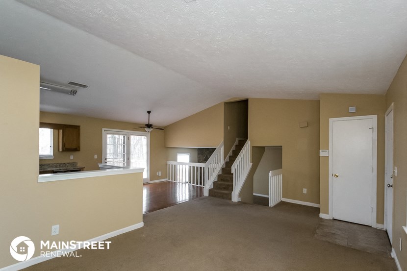 an empty living room with a staircase and a kitchen
