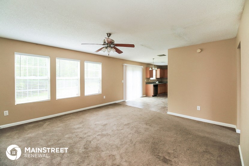 an empty living room with a ceiling fan and a kitchen