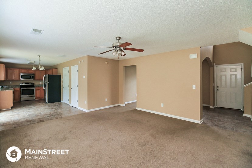 an empty living room with a ceiling fan and a kitchen