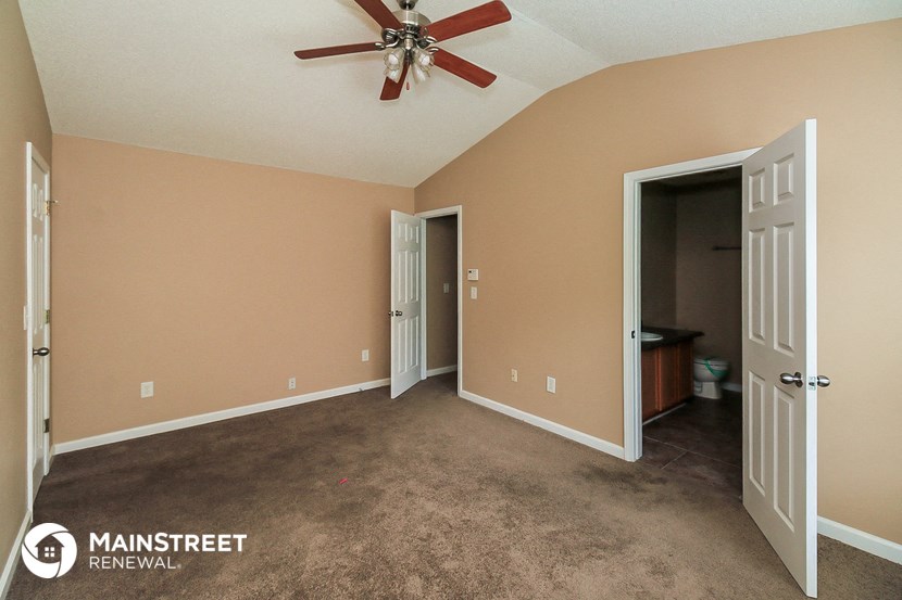 a carpeted room with a ceiling fan and a door to a bathroom