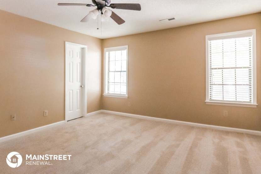 an empty living room with a ceiling fan and two windows