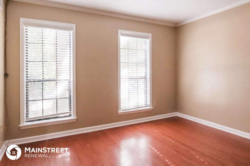 the living room of a home with wood floors and two windows
