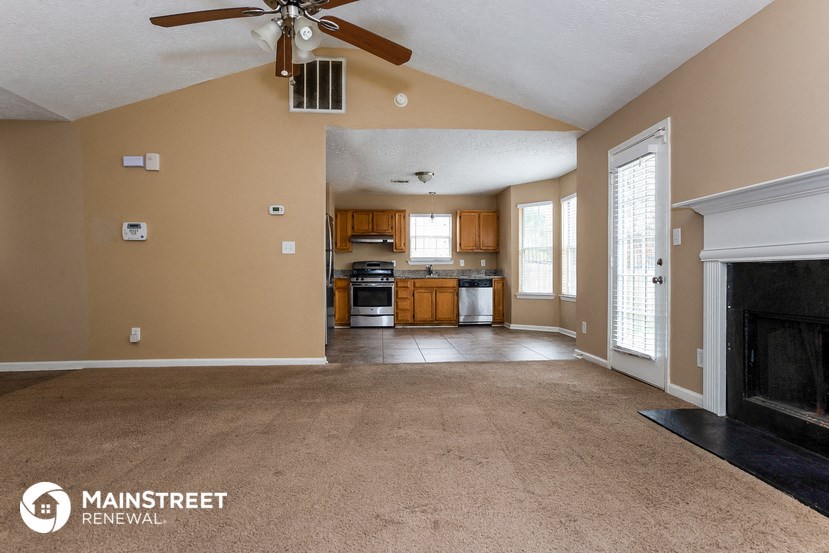 an empty living room with a ceiling fan and a kitchen
