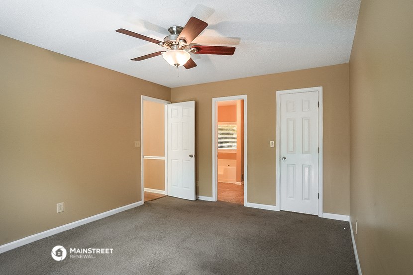 an empty living room with a ceiling fan and a door to a hallway