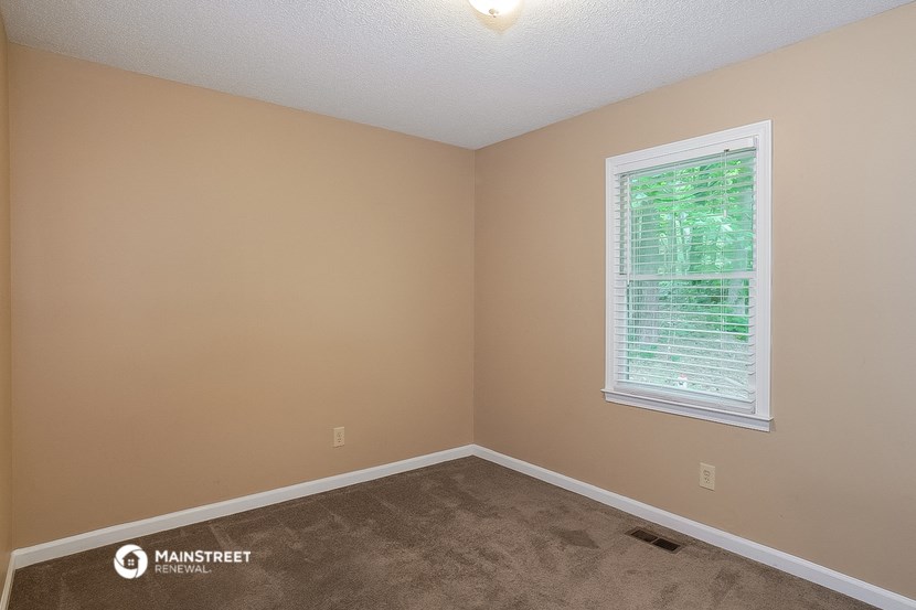 the bedroom of a house with carpet and a window