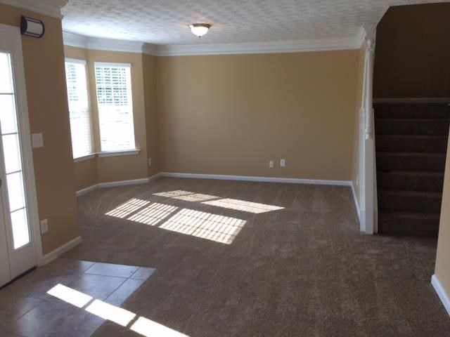 an empty living room with brown carpet and a staircase