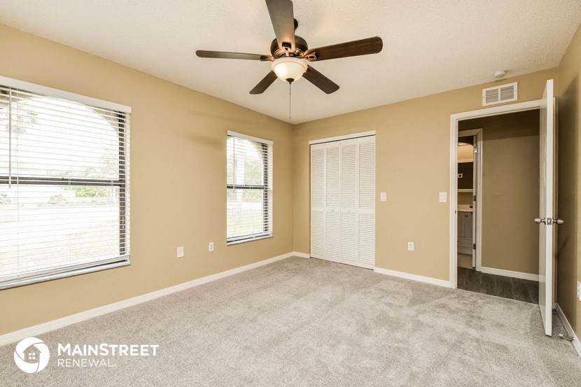 an empty living room with a ceiling fan and two windows