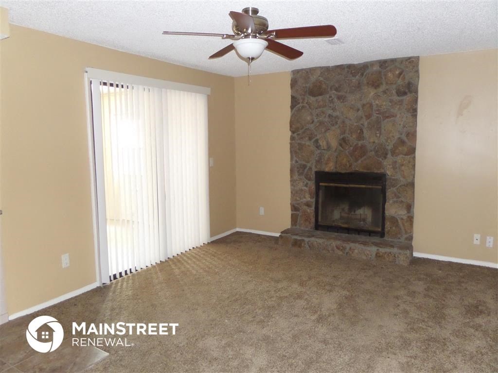 a living room with a stone fireplace and a ceiling fan