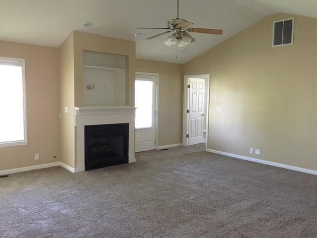 an empty living room with a fireplace and a ceiling fan