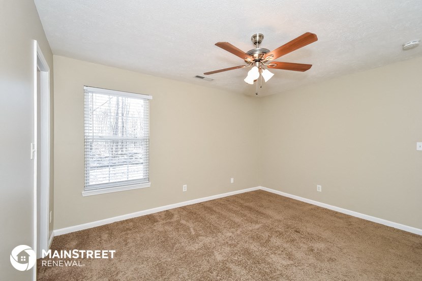 the spacious living room has carpet and a ceiling fan